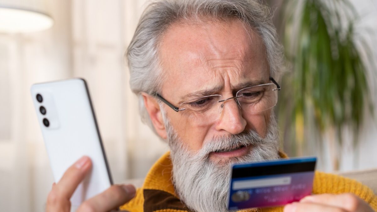 Senior answering a call while holding his card, part of 7 Common Scams Targeting Seniors.