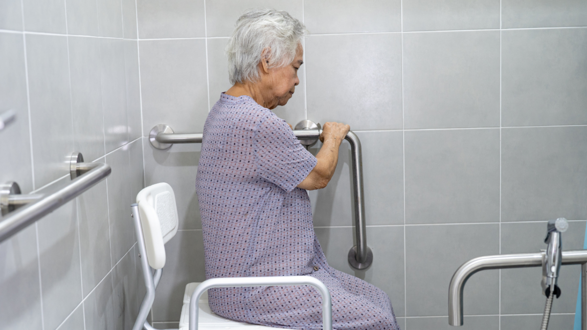 Senior woman sitting in the bathroom chair while holding in the grab bar, as Fall Prevention Strategies