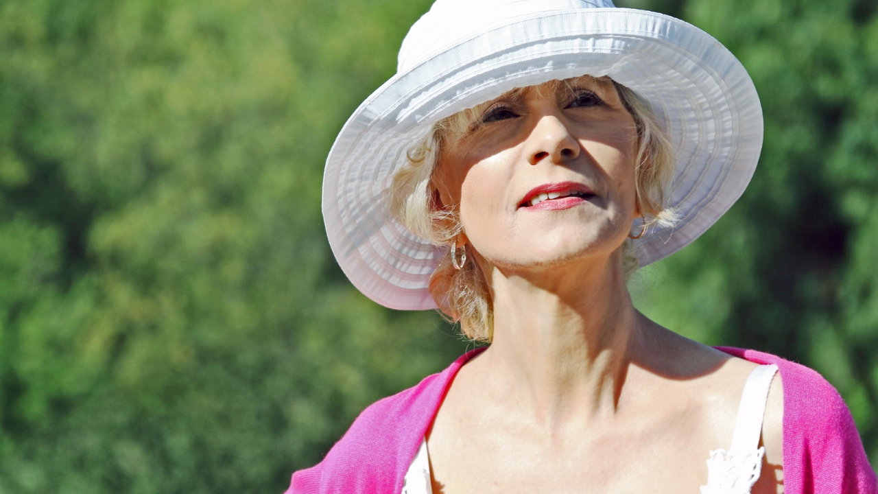 Senior woman using a hat as a summer heat tip to stay cool and healthy.