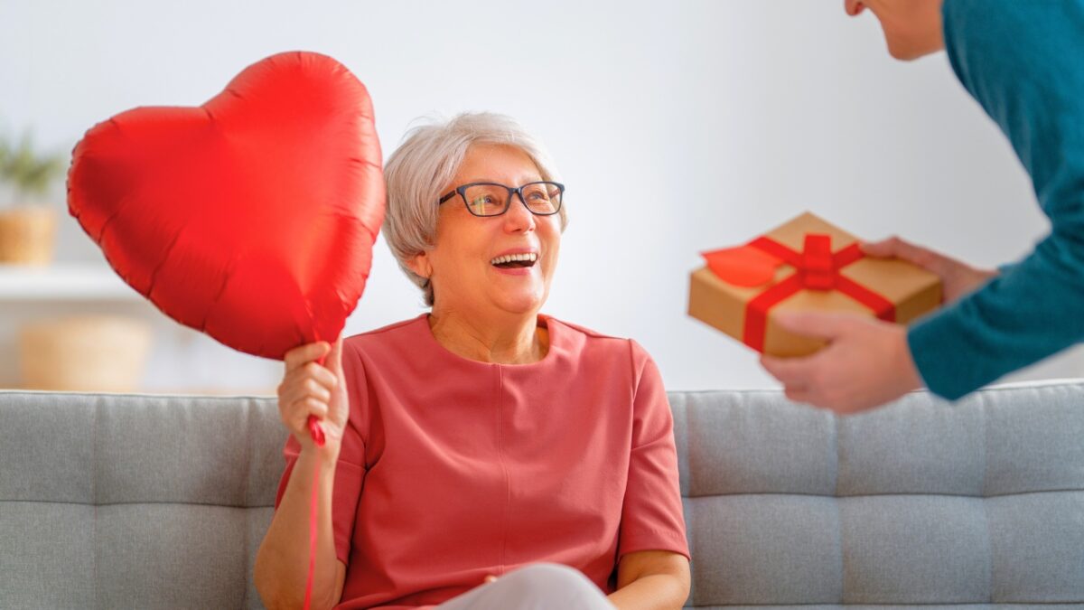 A senior woman holding a heart balloon and is receiving a Valentine's Day gift