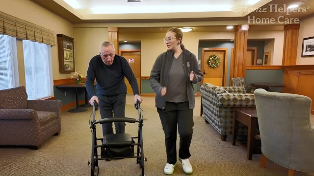 Senior client and caregiver walking inside assist living community