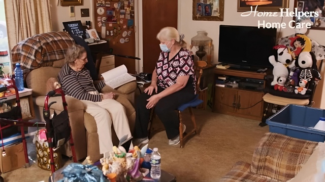 Caregiver accompanying senior woman who reads book.