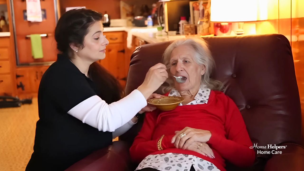 Home Helpers Home Health Aide doing personal care services at home, feeding a senior woman sitting on a couch.