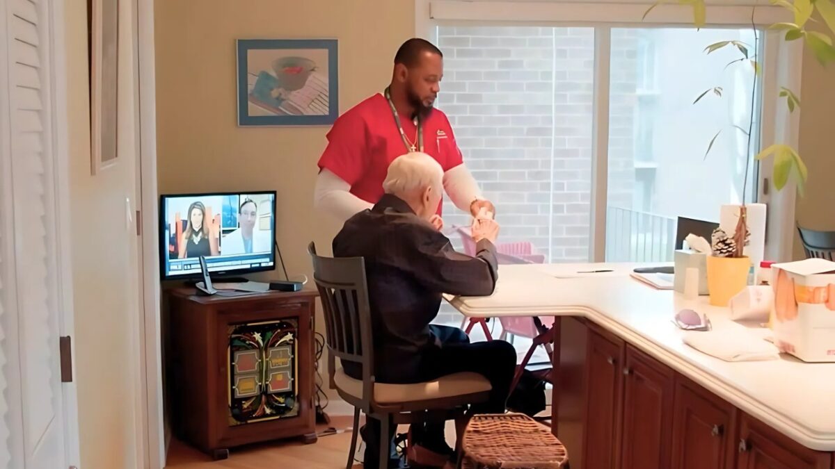 A caregiver in a red shirt is assisting an elderly person in the kitchen as part of the Benefits of In-Home Care.