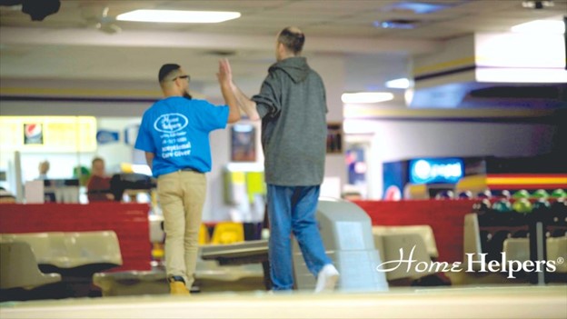 Caregiver and clients doing high five in a bowling place for mental wellness.