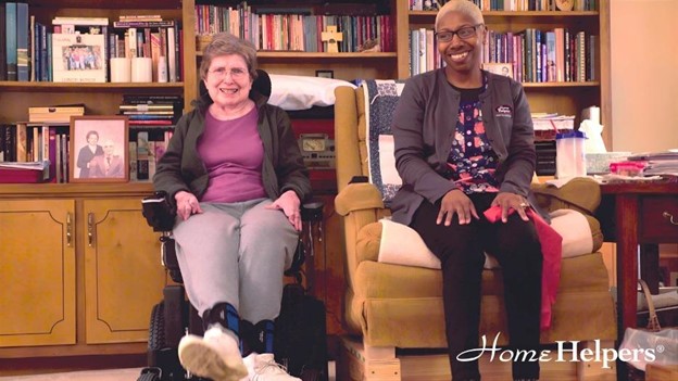 A senior in a wheelchair and a caregiver sitting in front of a bookshelf.