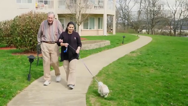 Senior and caregiver with the dog walking on the front yard as mental wellness for caregivers.