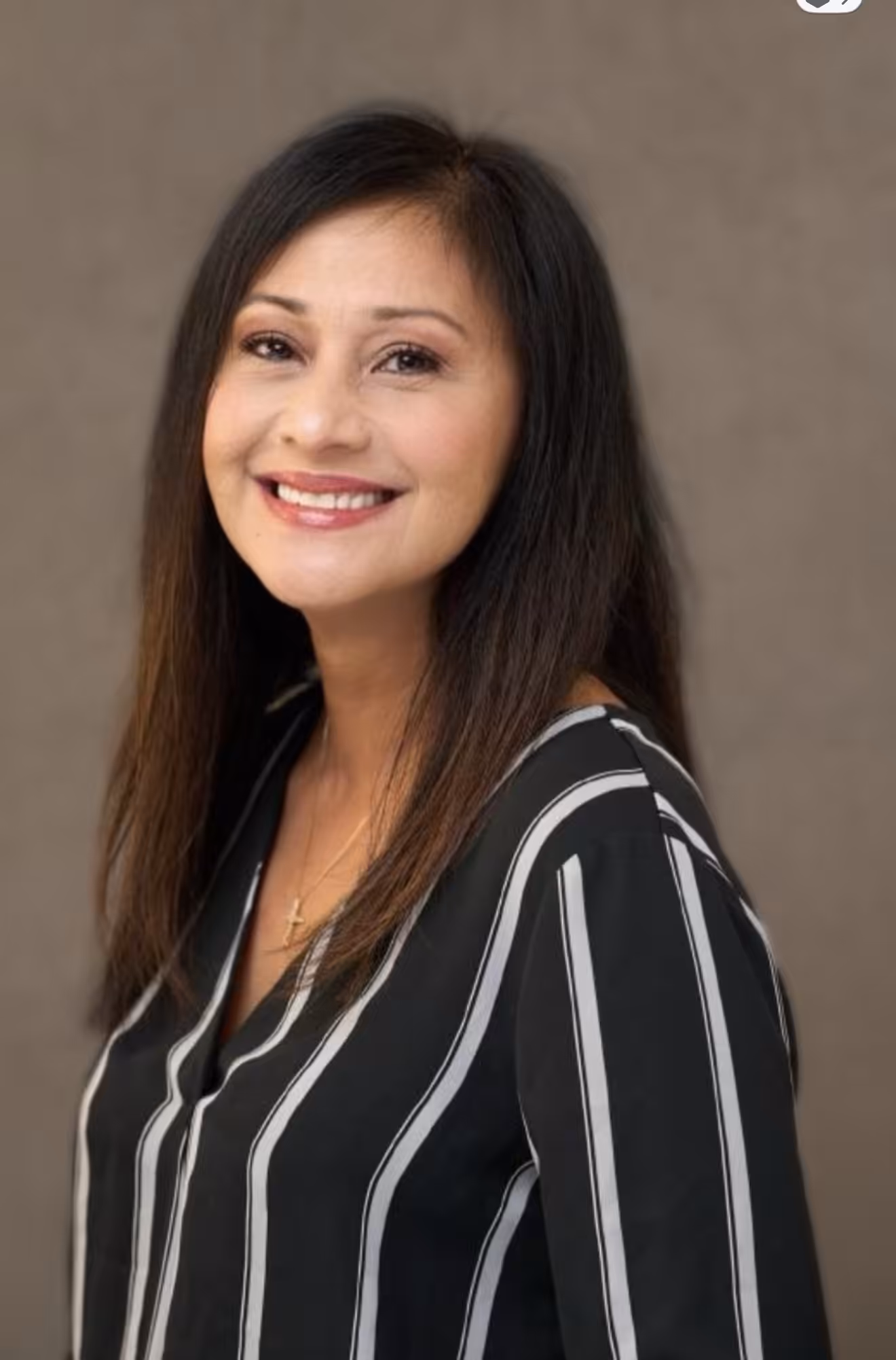 A woman with long, straight dark hair and a striped black blouse smiles at the camera against a plain, light brown background.