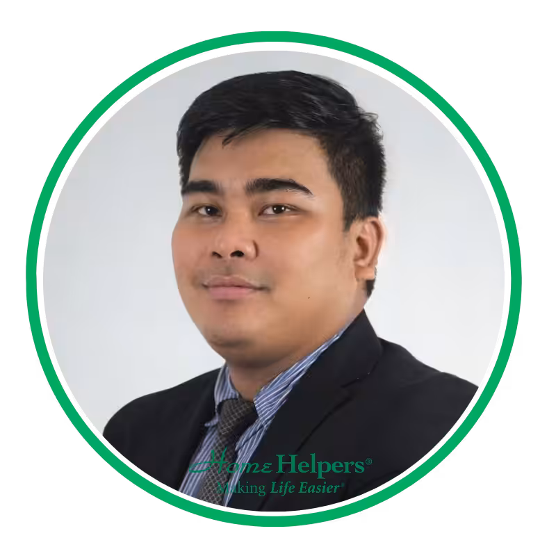 A man in a suit and tie poses for a professional headshot against a light background, framed by a green circle with the Franz Helpers logo and slogan Making Life Easier at the bottom.
