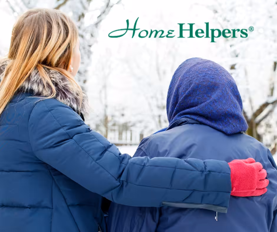 Two people in winter jackets walk outside in a snowy setting; one has a hand on the others back for support. The words Home Helpers appear at the top of the image.