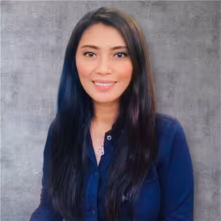 A woman with long, straight dark hair, wearing a navy blue button-up shirt, smiles at the camera against a gray textured background.