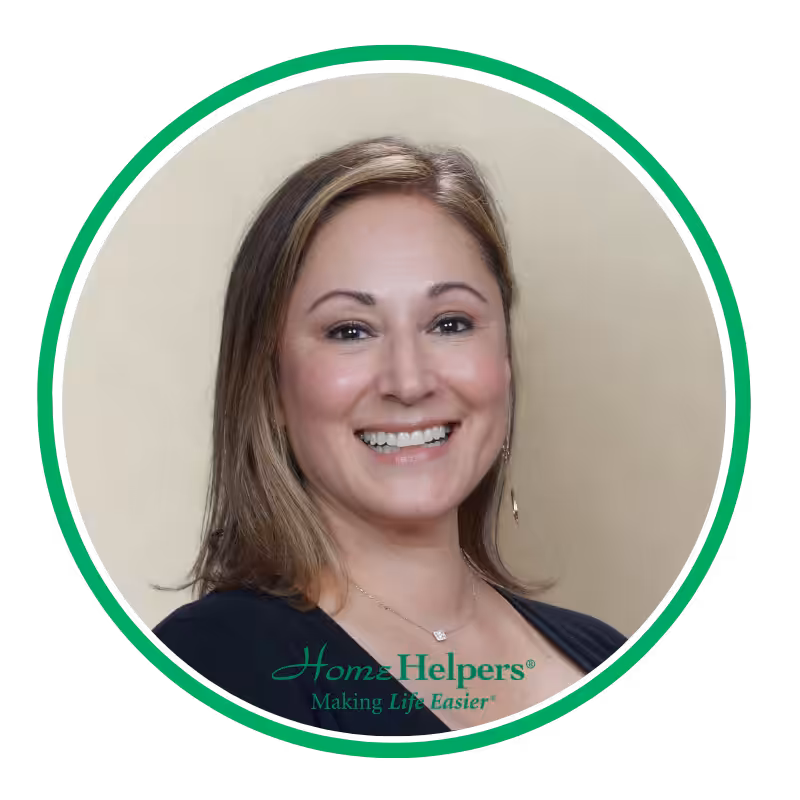 Smiling woman with shoulder-length light brown hair, wearing a black top and dangling earrings, posed in front of a beige background. “Home Helpers — Making Life Easier” logo appears at the bottom in green and teal.