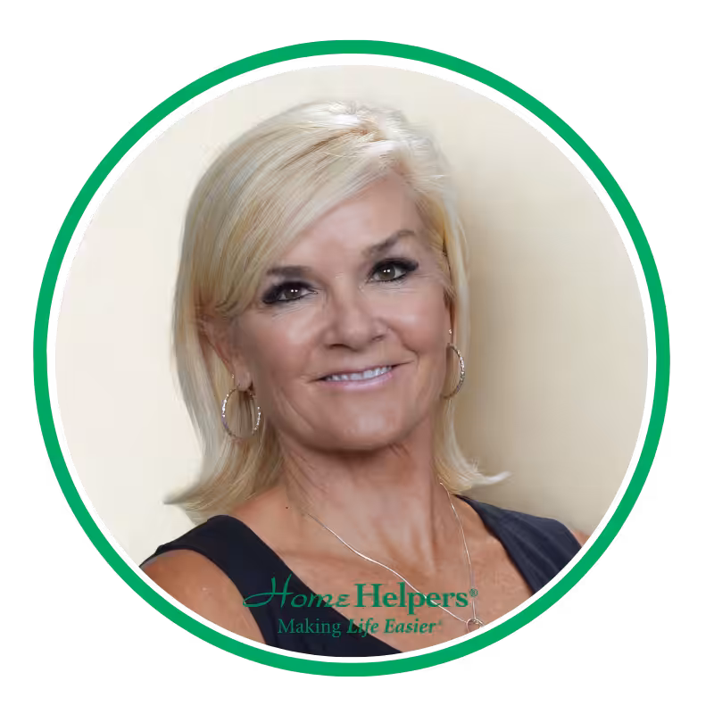 A smiling woman with short blonde hair wearing hoop earrings and a sleeveless black top, shown in a circular frame with a green border and the text “Home Helpers Making Life Easier” at the bottom.