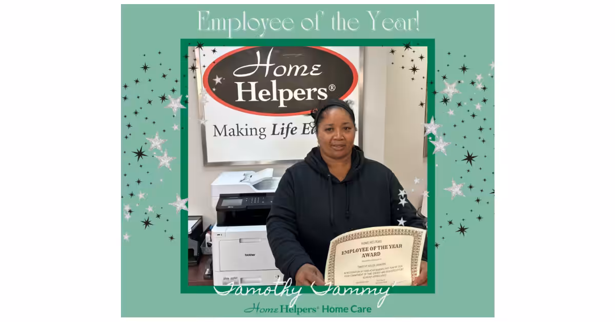 A woman stands in front of a “Home Helpers” sign holding an Employee of the Year award certificate, framed by a green border with sparkles and the text “Employee of the Year!” at the top.
