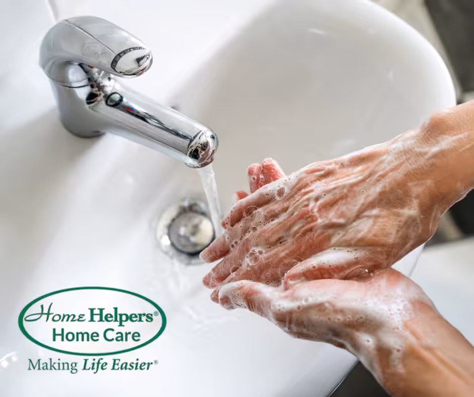 A person thoroughly washes their hands with soap under running water in a sink. The Home Helpers Home Care logo and the phrase Making Life Easier appear in the lower left corner.