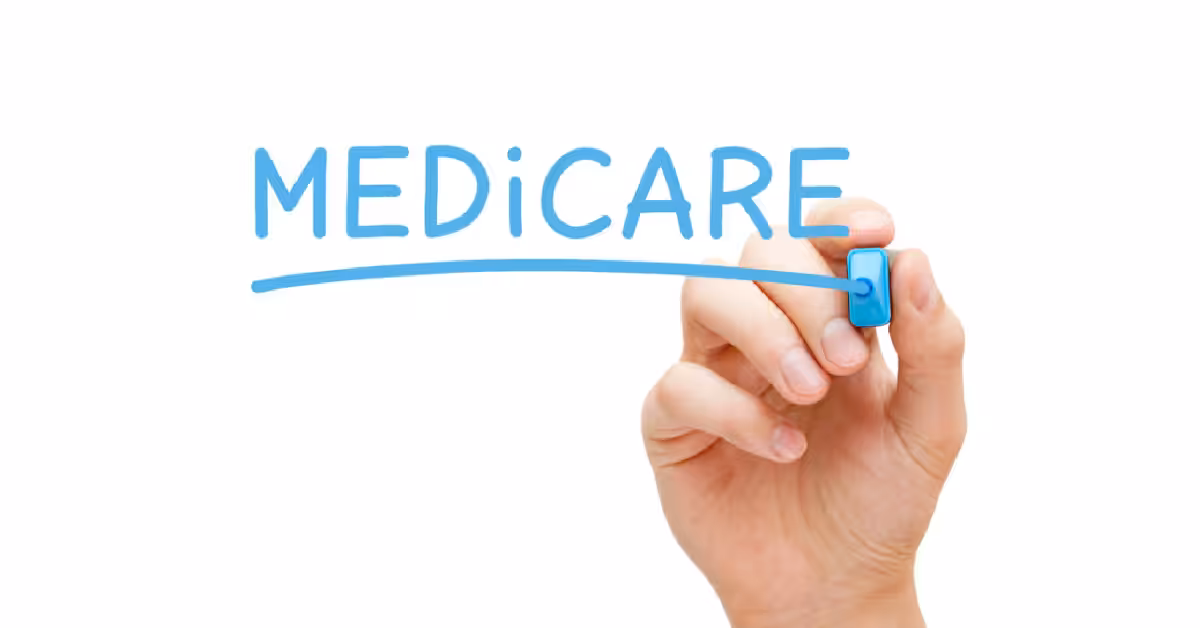 A hand holding a blue marker writes the word MEDICARE in large, blue letters on a clear surface with a line drawn underneath the word. The background is white.