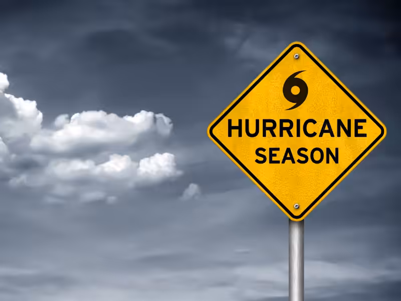 Yellow warning sign with a hurricane symbol and the words Hurricane Season against a cloudy, dark sky background.