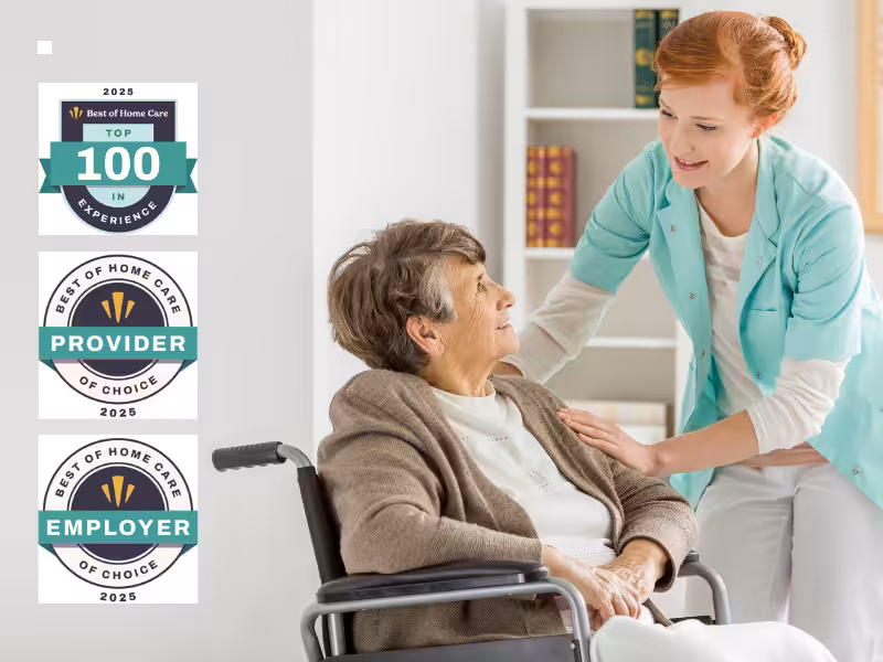 A smiling caregiver in a mint-green uniform gently talks to an elderly woman in a wheelchair. Three award badges for Best of Home Care 2025 appear on the left side of the image.