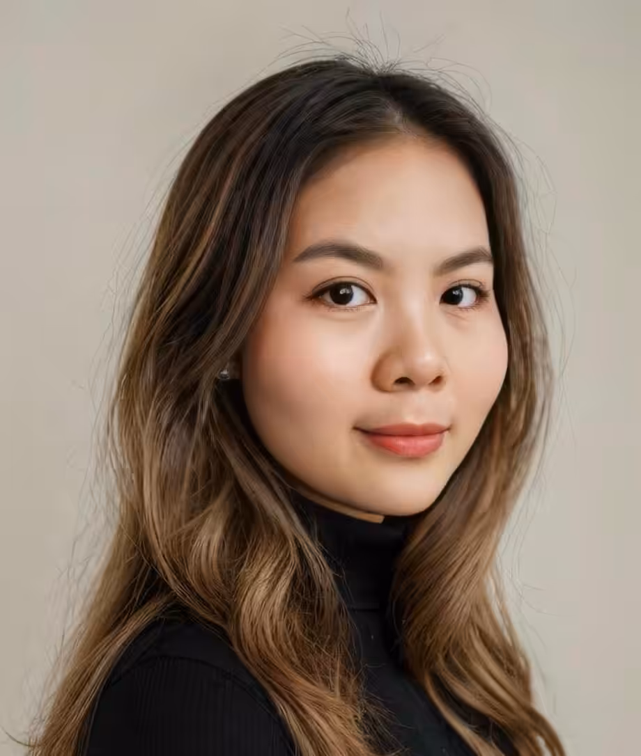 A young woman with long, wavy brown hair and natural makeup looks confidently at the camera. She is wearing a black turtleneck and the background is neutral and light-colored.