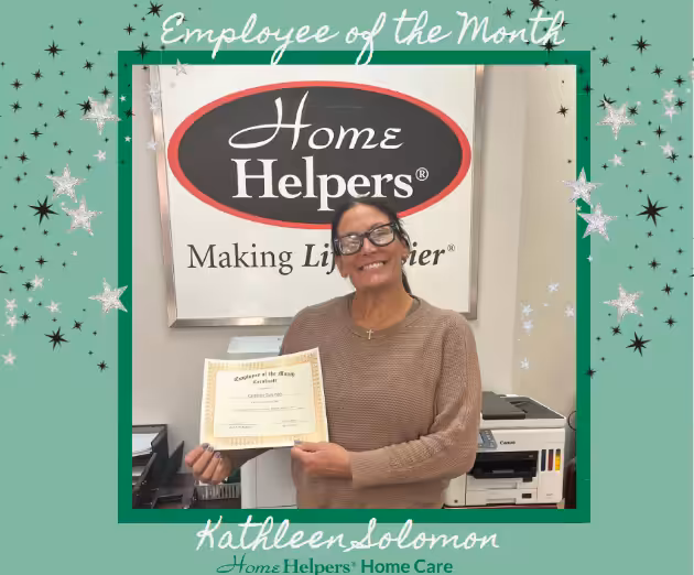 A woman smiles and holds an Employee of the Month certificate in front of a Home Helpers sign. The image is framed with green and white stars, with the text Employee of the Month and Kathleen Solomon, Home Helpers Home Care.