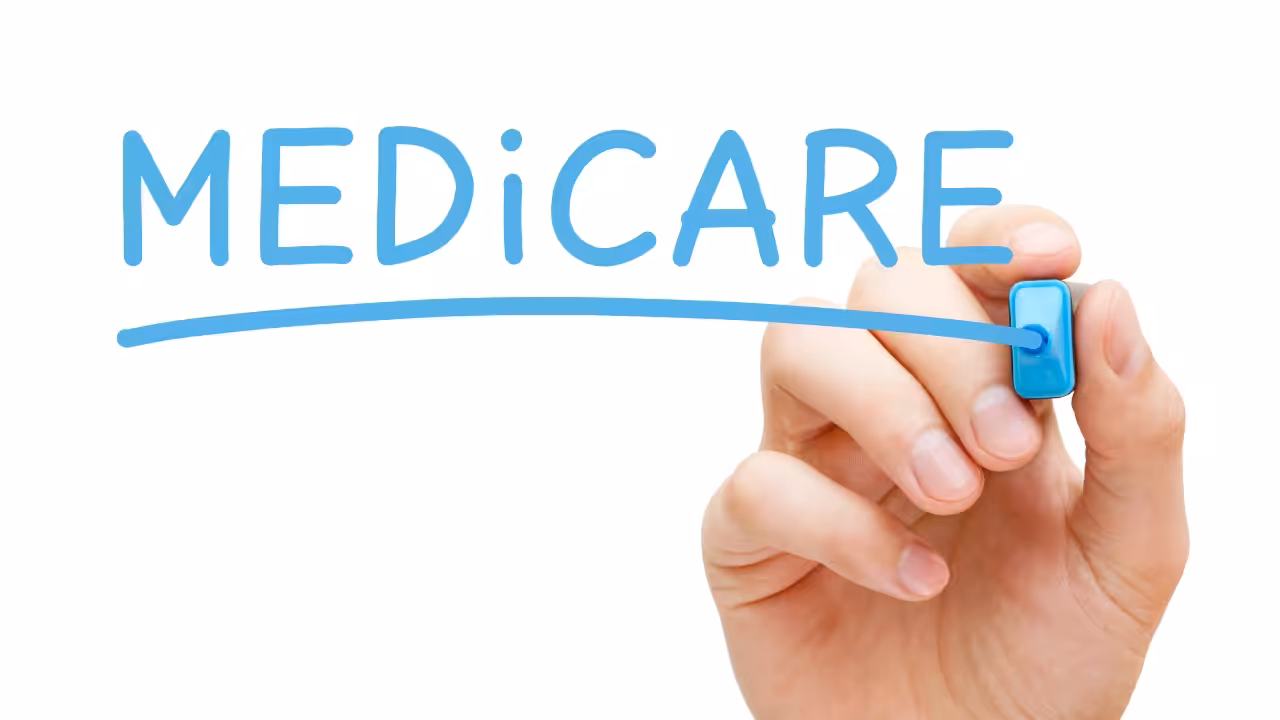A hand with a blue marker writes the word MEDICARE in large blue letters and underlines it on a white background.