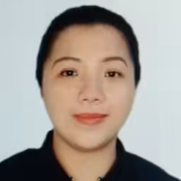 Portrait photo of a person with short dark hair, wearing a black collared top, and smiling softly against a plain light background.