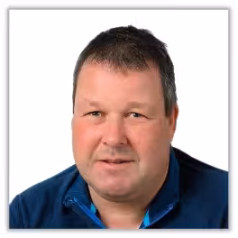 A middle-aged man with short dark hair wearing a blue zip-up jacket, facing the camera and smiling slightly, against a plain white background.