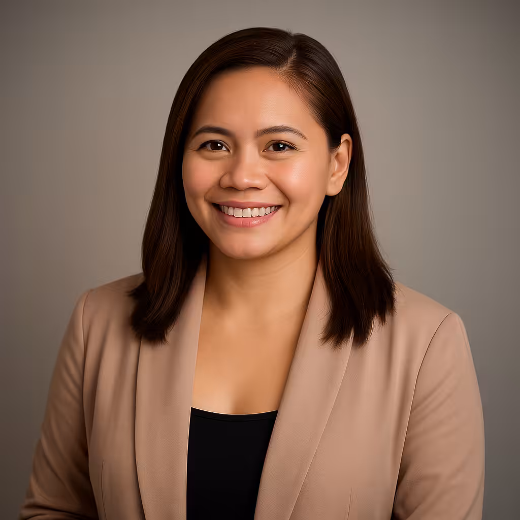 A woman with straight, shoulder-length brown hair smiles at the camera. She is wearing a beige blazer over a black top and is posed against a plain, neutral background.