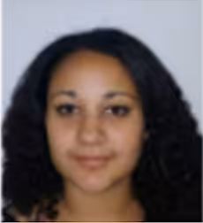 A woman with medium skin tone and curly dark hair is facing the camera and smiling slightly against a plain background.