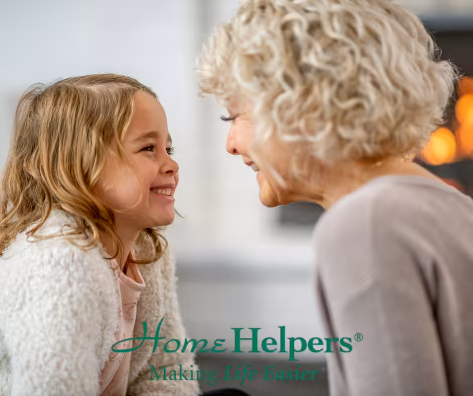 A smiling young girl and an elderly woman sit close together, looking at each other warmly. The text Home Helpers® Making Life Easier is displayed at the bottom of the image.
