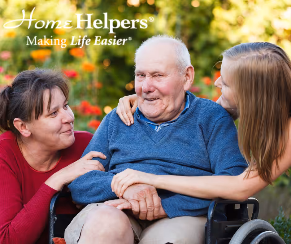 An elderly man in a wheelchair sits outside, smiling and holding hands with two happy women at his side. The text reads, Home Helpers® Making Life Easier®. Bright flowers fill the background.