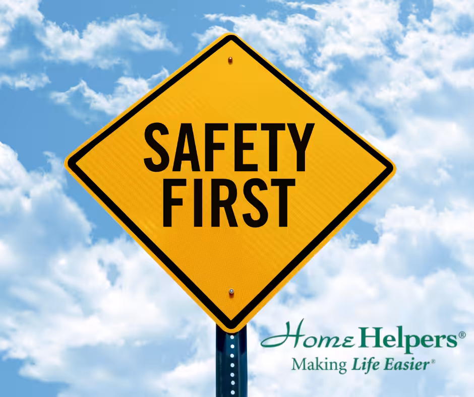 A yellow diamond-shaped road sign reads SAFETY FIRST against a blue sky with clouds. In the bottom right corner is the Home Helpers logo with the tagline Making Life Easier.