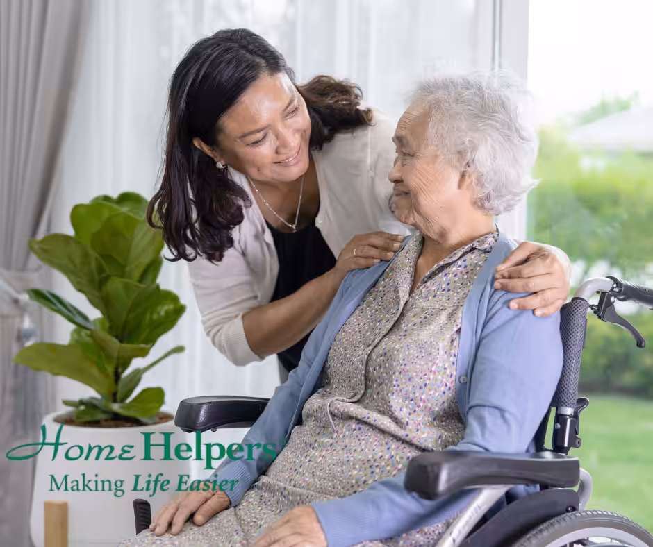 A smiling caregiver stands behind an elderly woman in a wheelchair, gently touching her shoulders. Both women look at each other warmly. The text reads: Home Helpers - Making Life Easier. A green plant is nearby.