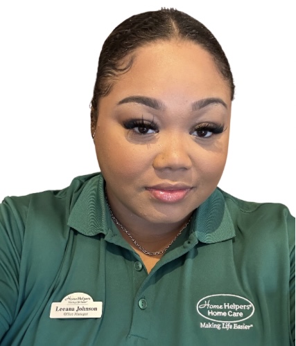 A woman with neatly styled hair wears a green Home Helpers Home Care polo shirt and name badge. She is looking at the camera with a slight smile.