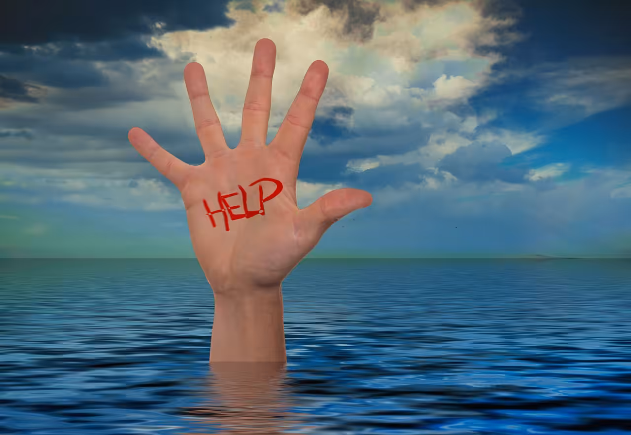 A hand rising out of water with the word HELP written in red on its palm, against a backdrop of a cloudy sky and blue water, symbolizing a call for assistance or distress.