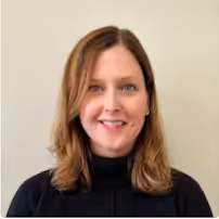 A woman with shoulder-length light brown hair, wearing a black turtleneck sweater, smiles at the camera against a plain light-colored background.