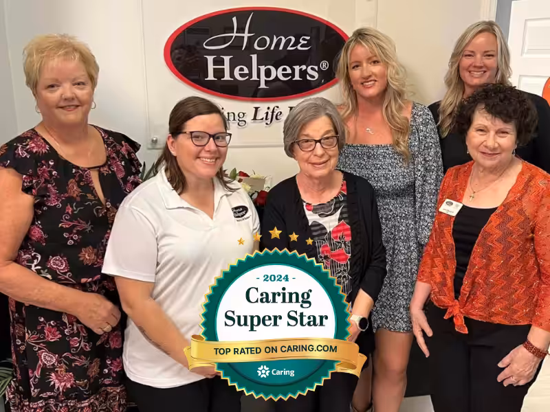 Six smiling women pose indoors in front of a Home Helpers sign. One woman holds a 2024 Caring Super Star award badge, recognizing top ratings on Caring.com.