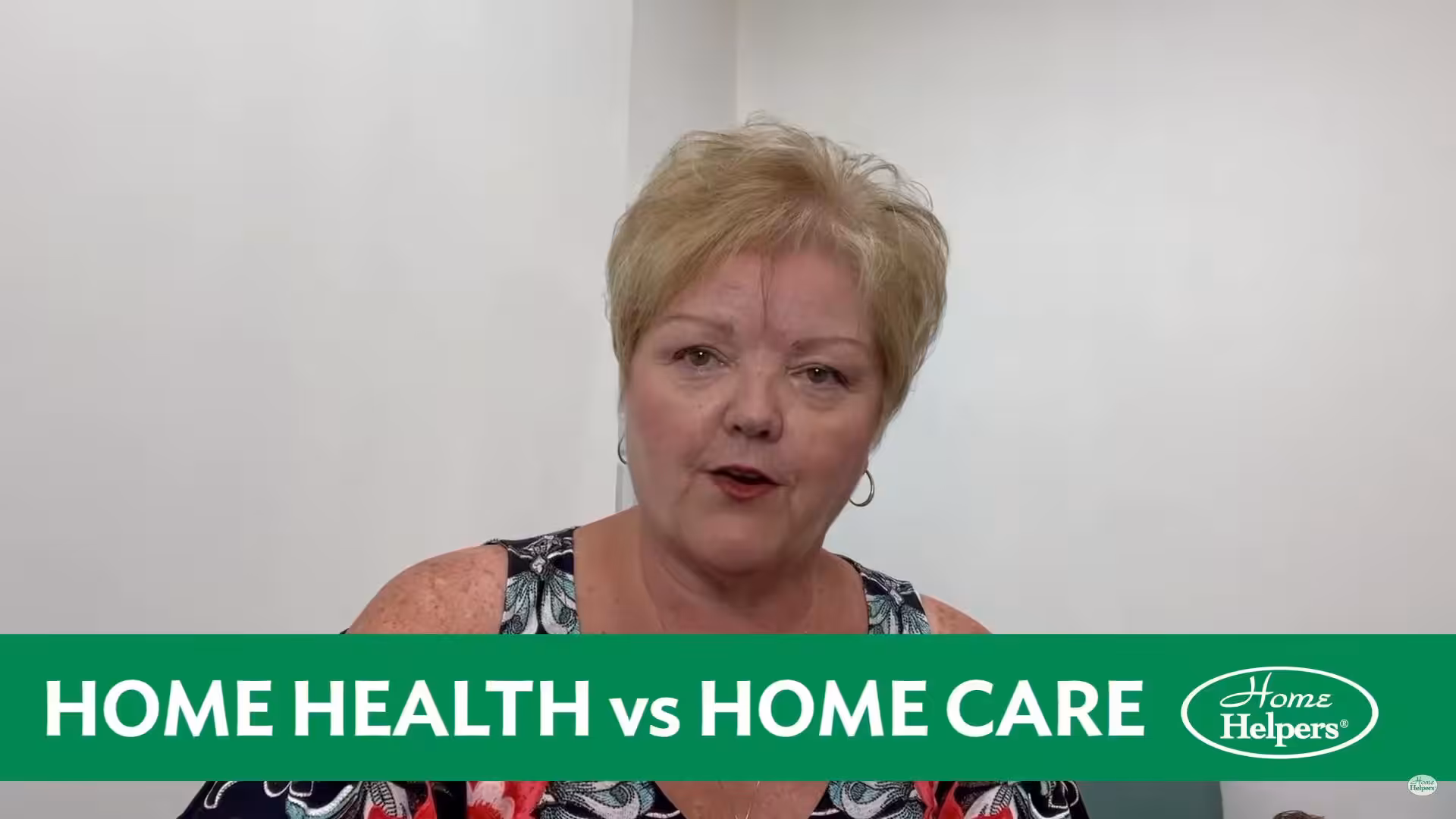 A woman with short blond hair sits against a plain white wall. A green banner at the bottom reads HOME HEALTH vs HOME CARE with the Home Helpers logo.