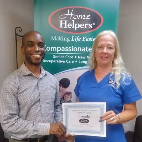 Two people stand in front of a Home Helpers banner. The woman on the right holds a certificate that reads Exceptional Employee of the Month, September 2018, Brenda. Both are smiling at the camera.