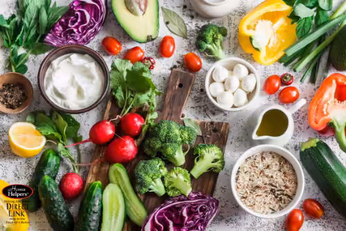 A colorful assortment of fresh vegetables, rice, mozzarella balls, herbs, and olive oil arranged on a table, including broccoli, cucumbers, radishes, bell peppers, tomatoes, purple cabbage, and a bowl of yogurt.