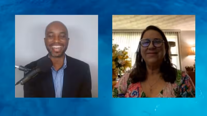 Two people are on a video call. The man on the left is smiling, wearing a suit jacket, and has a microphone. The woman on the right is wearing glasses and a colorful top, also smiling. Both have indoor backgrounds.