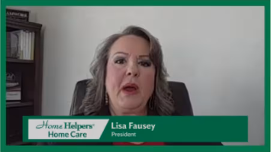 A woman with shoulder-length gray hair sits in an office chair, speaking on camera. A graphic at the bottom reads Home Helpers Home Care and identifies her as Lisa Fausey, President.