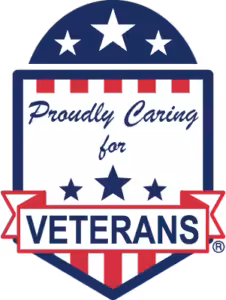 A shield-shaped badge with stars and stripes reads Proudly Caring for VETERANS in bold letters, using red, white, and blue patriotic colors.