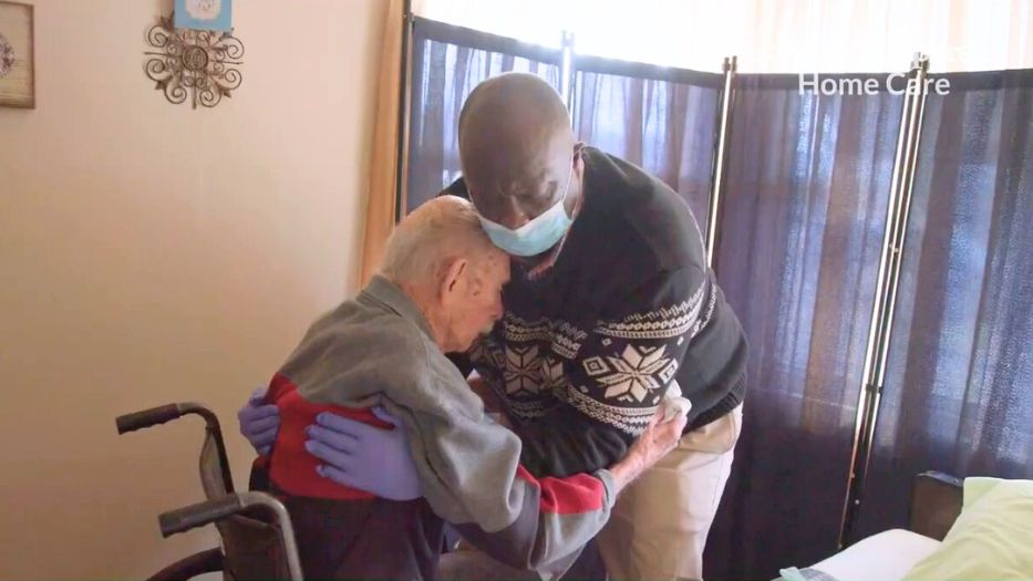 Caregivers assist with the transfer of a senior from a wheelchair to a bed