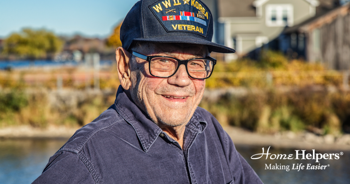 An older man in glasses and a Korea Veteran cap smiles outdoors by a waterfront. He wears a dark shirt. Home Helpers: Making Life Easier is written in the bottom right corner.