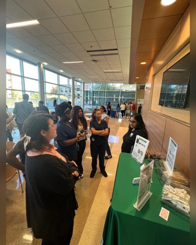 A group of people standing around a table with information brochures and supplies in a bright, modern building lobby.
