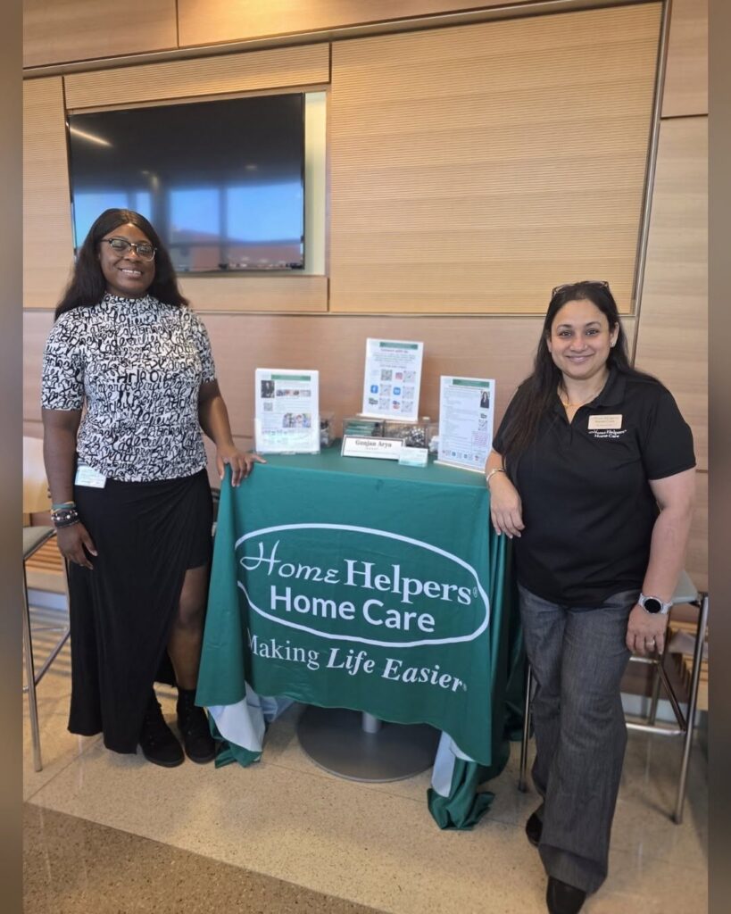 Two women stand on either side of a display table for Home Helpers Home Care.