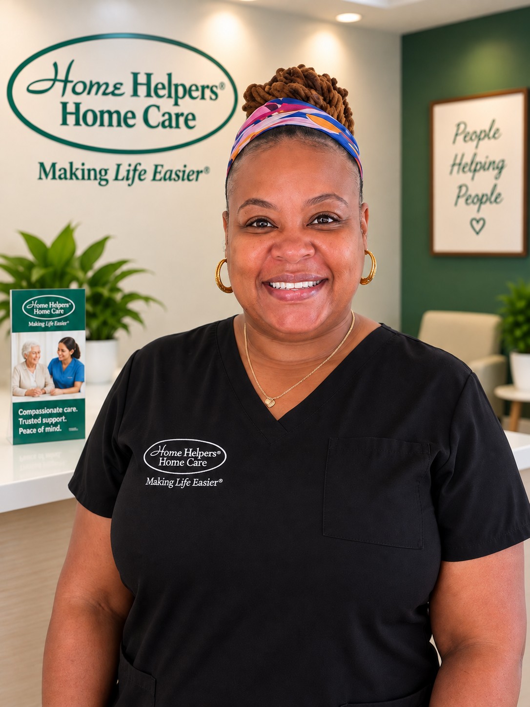 A smiling woman wearing a black Home Helpers Home Care uniform stands in an office with the company logo on the wall behind her.