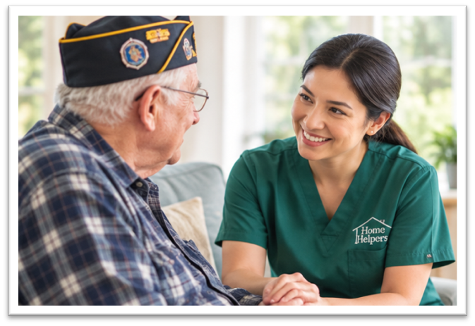 A female caregiver in a green uniform smiles while holding the hands of an elderly man wearing a veterans cap.