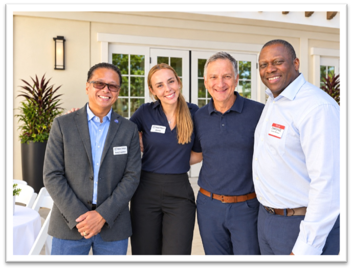 Four people standing together outdoors, smiling for a group photo.